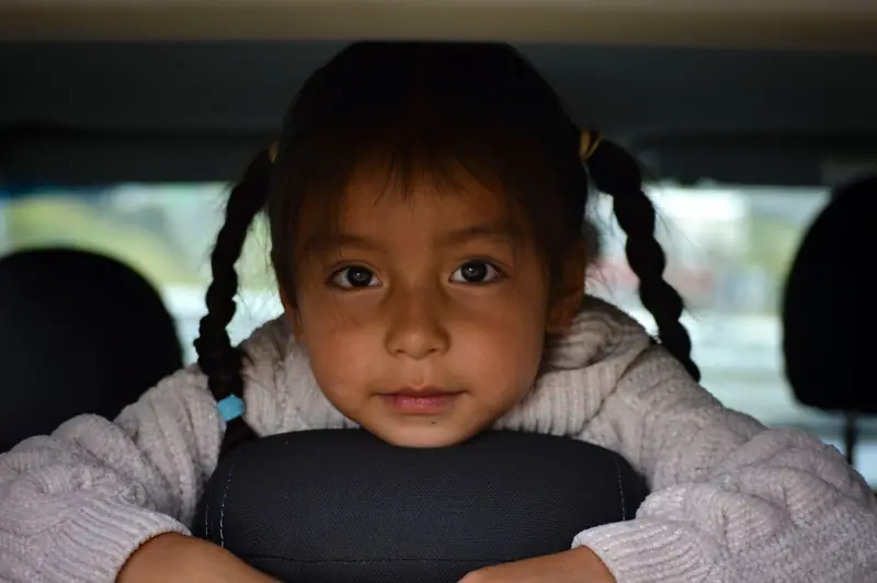 A young girl with braids smiling from the back seat of a car