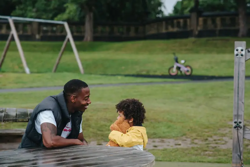 A father and his young son laughing together at a park table