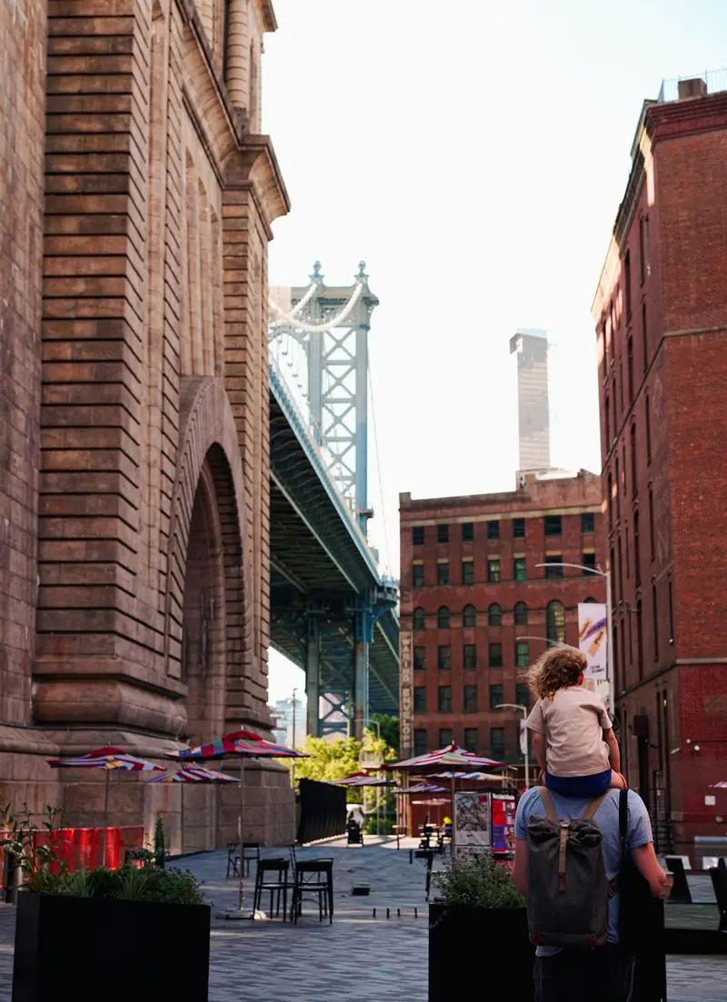 A father carrying his child on his shoulders on a Brooklyn street near the Manhattan Bridge
