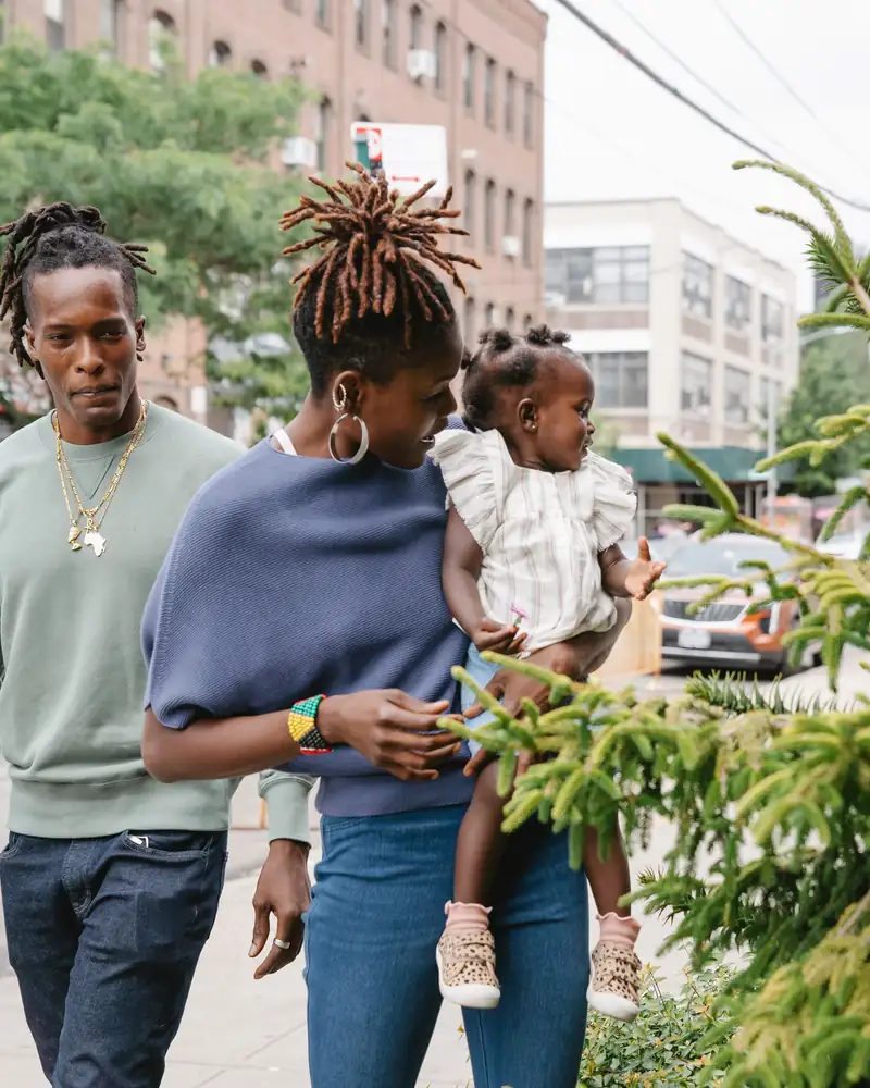 A young couple holding their toddler on a city sidewalk lined with brick buildings