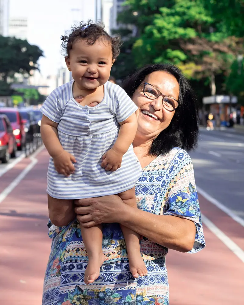 A grandmother laughing as she holds up her grandchild on a city street
