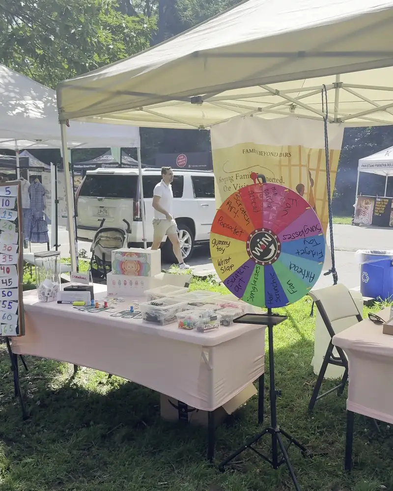 The Families Beyond Bars booth on July 19, with a prize wheel and tables under a white tent in Prospect Park
