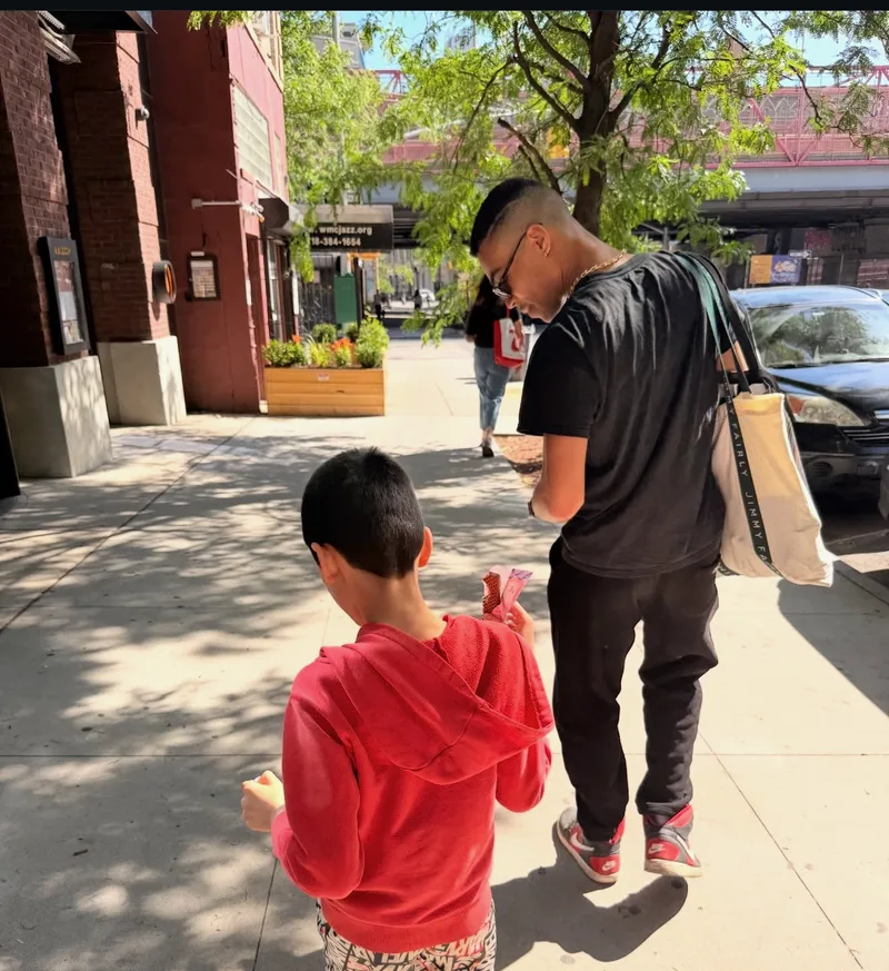 A volunteer and a young boy walking down a Brooklyn sidewalk with flyers