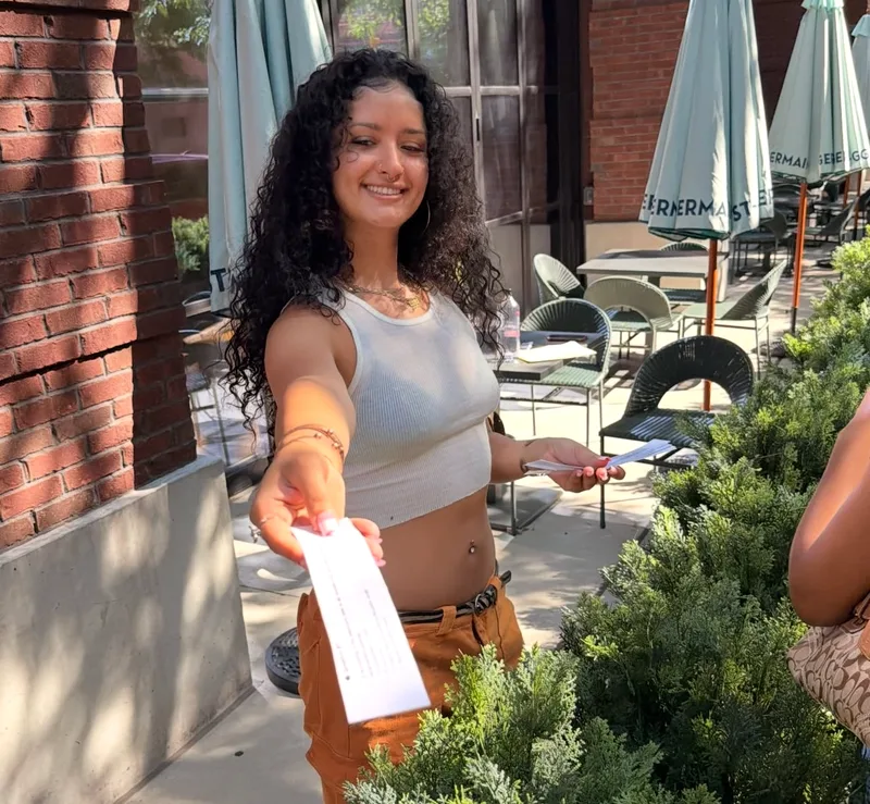 A volunteer smiling and handing out a flyer on an outdoor patio