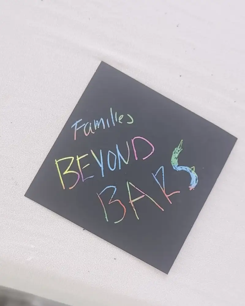 A hand-lettered Families Beyond Bars sign in rainbow chalk on a black card